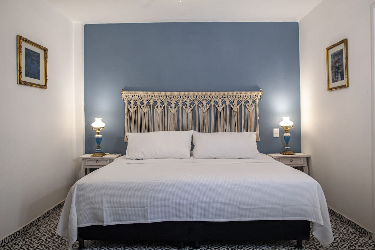 Un dormitorio con una cama, dos mesitas de noche y dos lámparas de pared.