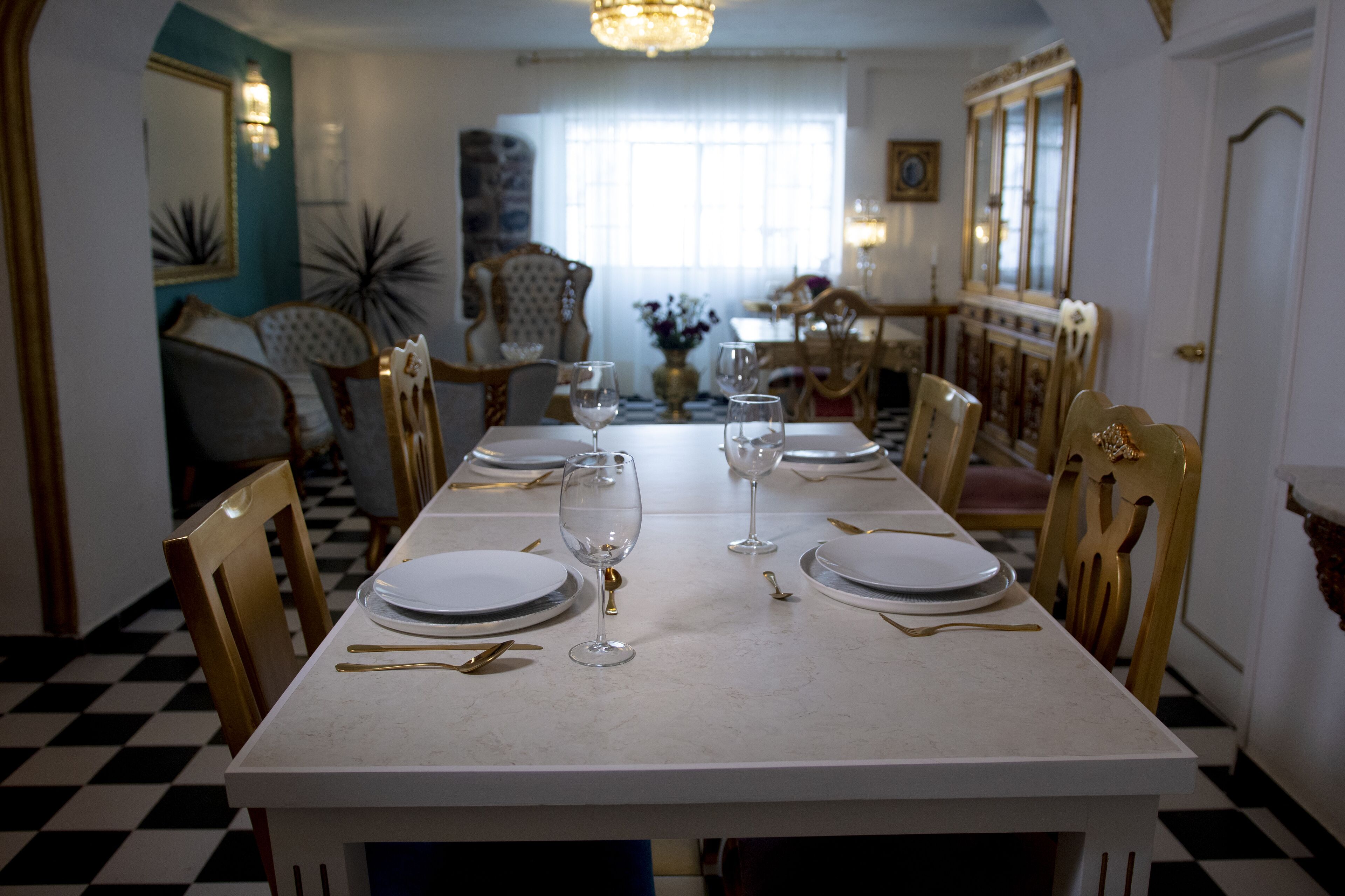 A dining room with a checkered floor, a white table set with plates, glasses, and cutlery.