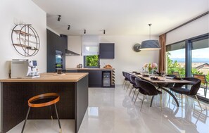 Enjoy meals in the spacious kitchen with a central island, oven, and wine rack, adjacent to a dining area with a long table and chandelier.