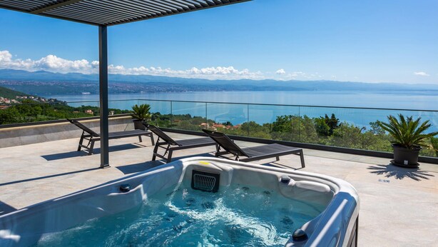 Eine Dachterrasse mit Whirlpool, Liegestühlen und einem schönen Blick auf See und Berge.