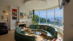 A modern living room with a curved green sofa, a fireplace, and a large window offering a scenic view. - Amazing home in Kostrena with sauna (Kostrena)