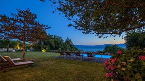 A pool area with lounge chairs, a wooden deck, and a view of the sea at dusk. - Amazing home in Kostrena with sauna (Kostrena)