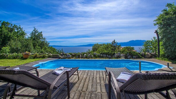 A wooden deck with lounge chairs and a swimming pool overlooking a body of water with mountains in the distance. - Amazing home in Kostrena with sauna (Kostrena)