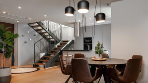 A modern kitchen with a central island, a dining area with brown leather chairs, and a staircase leading to an upper level. - Lovely home in Labin - Rabac (Labin - Rabac)