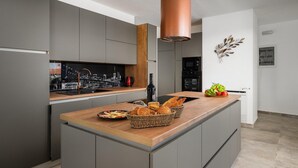 Une cuisine moderne avec des meubles gris, un plan de travail en bois et une hotte de cuisinière en cuivre. Une fenêtre située au-dessus de l’évier offre une vue sur le paysage urbain, et un panier de fruits est posé sur le plan de travail.