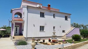 A two-story building with a white facade, a small balcony, and a stone fountain in the courtyard. - Holiday apartment with air conditioning (Peroj)