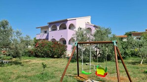 A playground with swings in front of a multi-story building with arched windows. - Holiday apartment with air conditioning (Peroj)