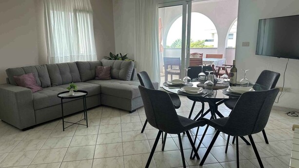 Un soggiorno moderno con un divano angolare grigio, un tavolino e un'area pranzo con un tavolo rotondo e sedie.