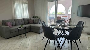 En moderne stue med en grå hjørnesofa, et lille rundt bord med en plante, og et spiseområde med et rundt bord og stole.