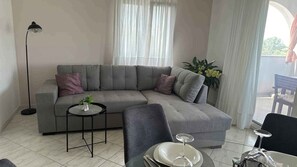 En moderne stue med en grå hjørnesofa, et lille rundt bord og et spiseområde med en stol og et glastop bord.
