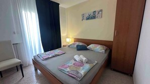 Una camera d'albergo con un letto, una sedia, un comodino con una lampada e una porta.