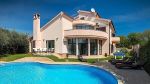 Uma casa moderna de dois andares com piscina, área de estar externa e um grande portão de vidro.