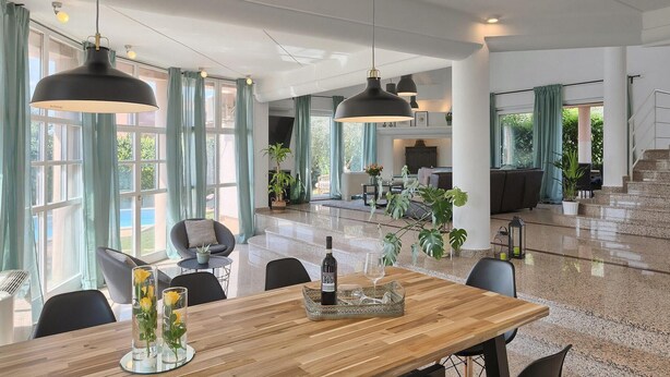 Uma ampla área de refeições com mesa de madeira, cadeiras e luminárias pendentes.