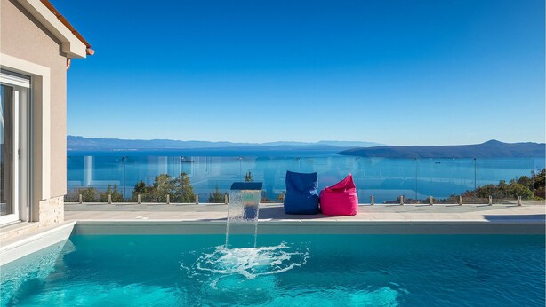 Ein Schwimmbecken mit freiem Blick auf den Ozean und Berge im Hintergrund.