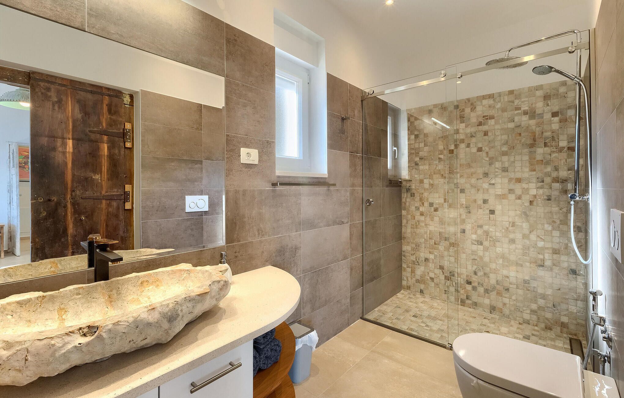 A modern bathroom with a stone sink, a glass shower enclosure, and a large mirror.