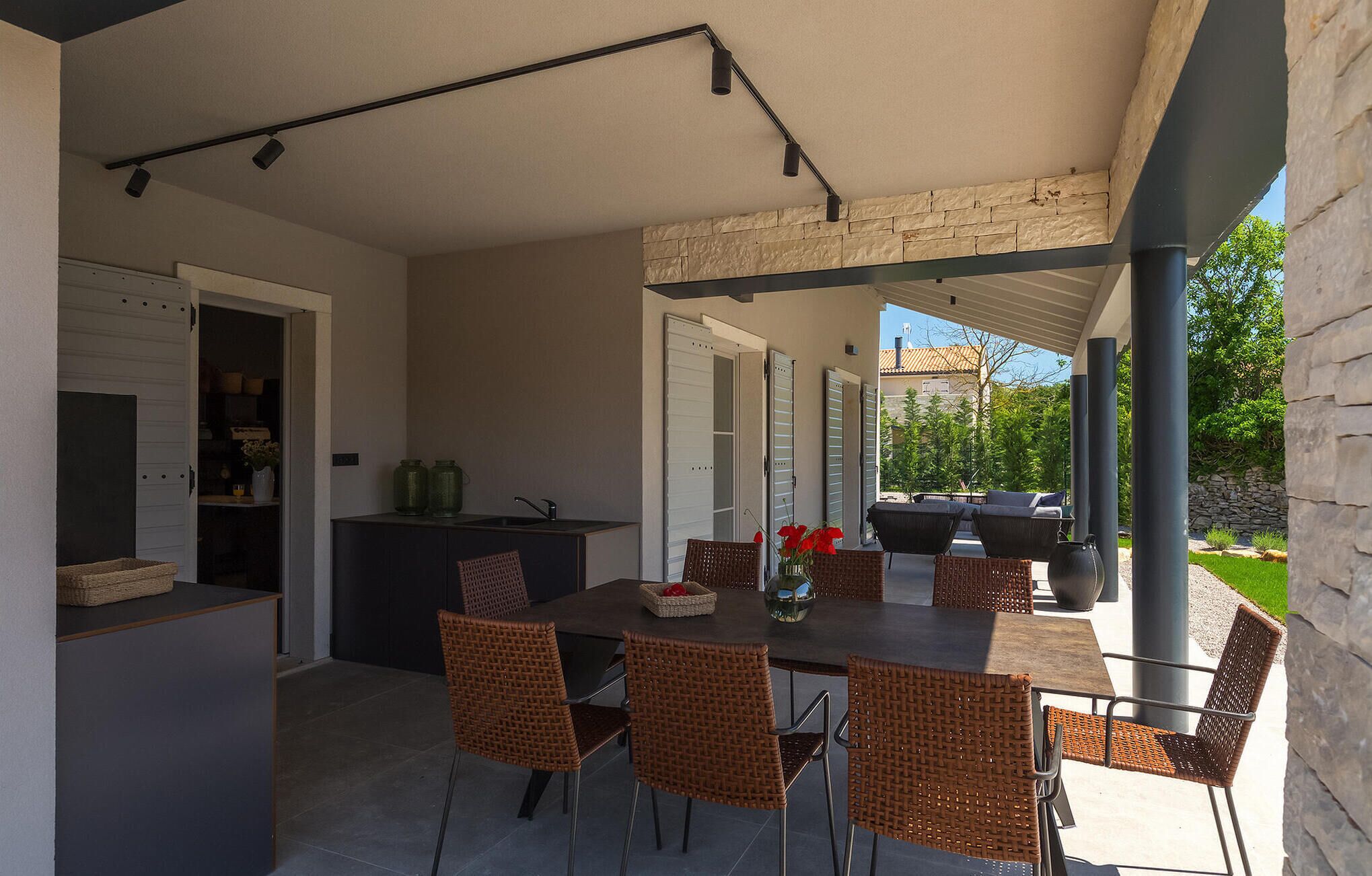 Un área de comedor al aire libre con techo, sillas de mimbre y una mesa, una cocina con horno empotrado y una pared de piedra.