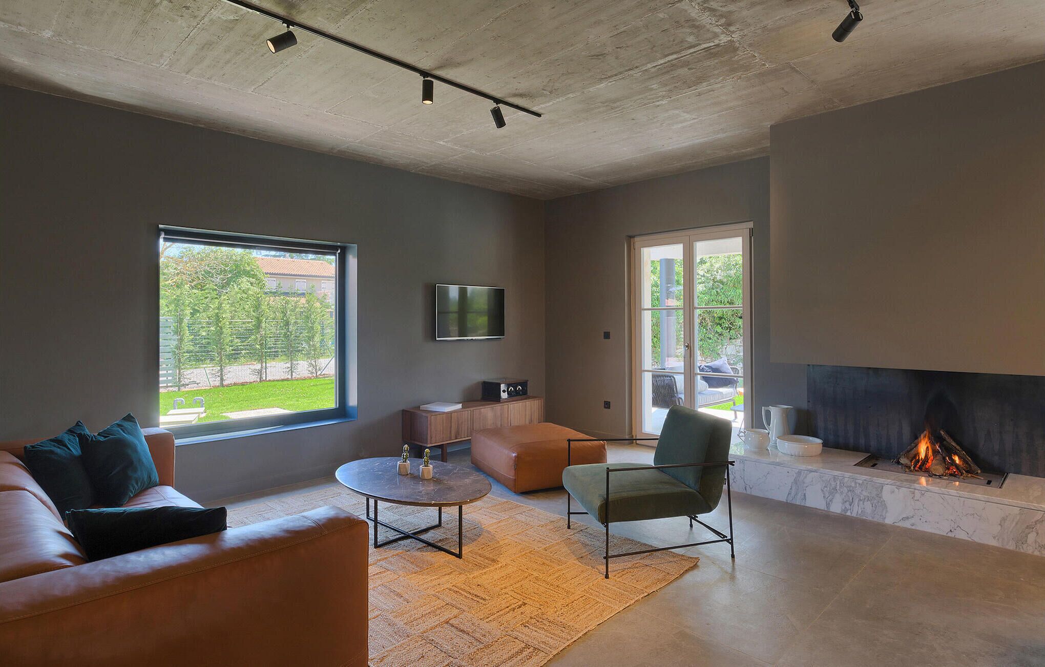 A modern living room with a sofa, armchair, coffee table, fireplace, TV, and large windows.
