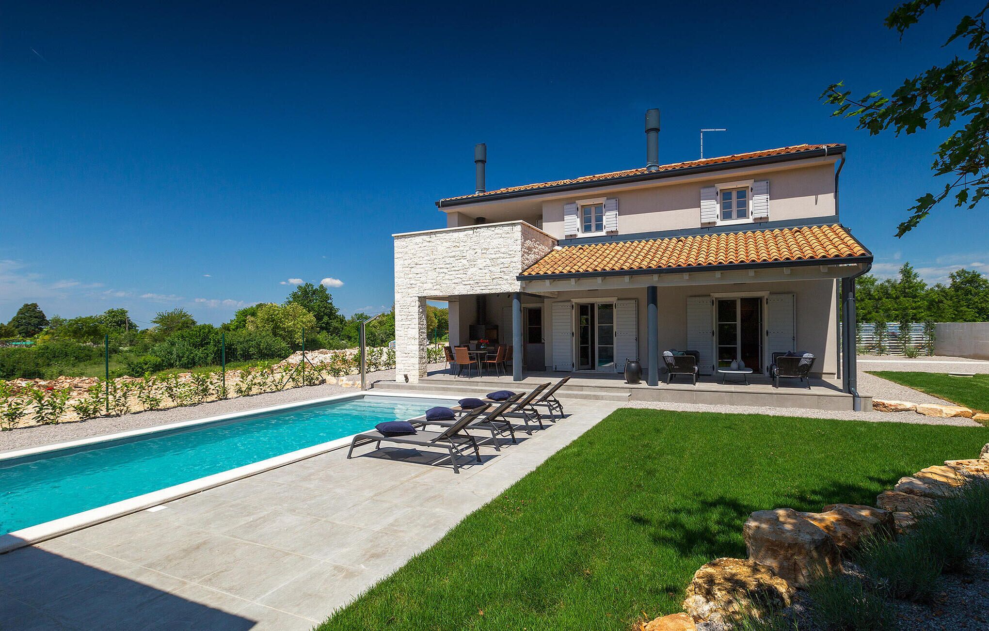 A two-story house with a swimming pool, outdoor seating, and a garden.