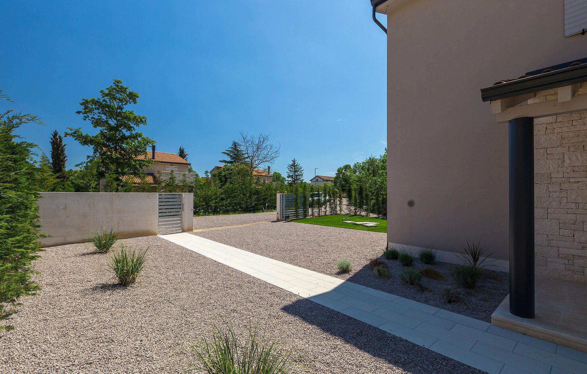 A modern building with a gravel driveway, a concrete pathway, and a small lawn area.