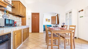 A kitchen with wooden cabinets, a microwave, and a dining table with chairs. - La Casa Azzurra with shared Pool (Tertenia)