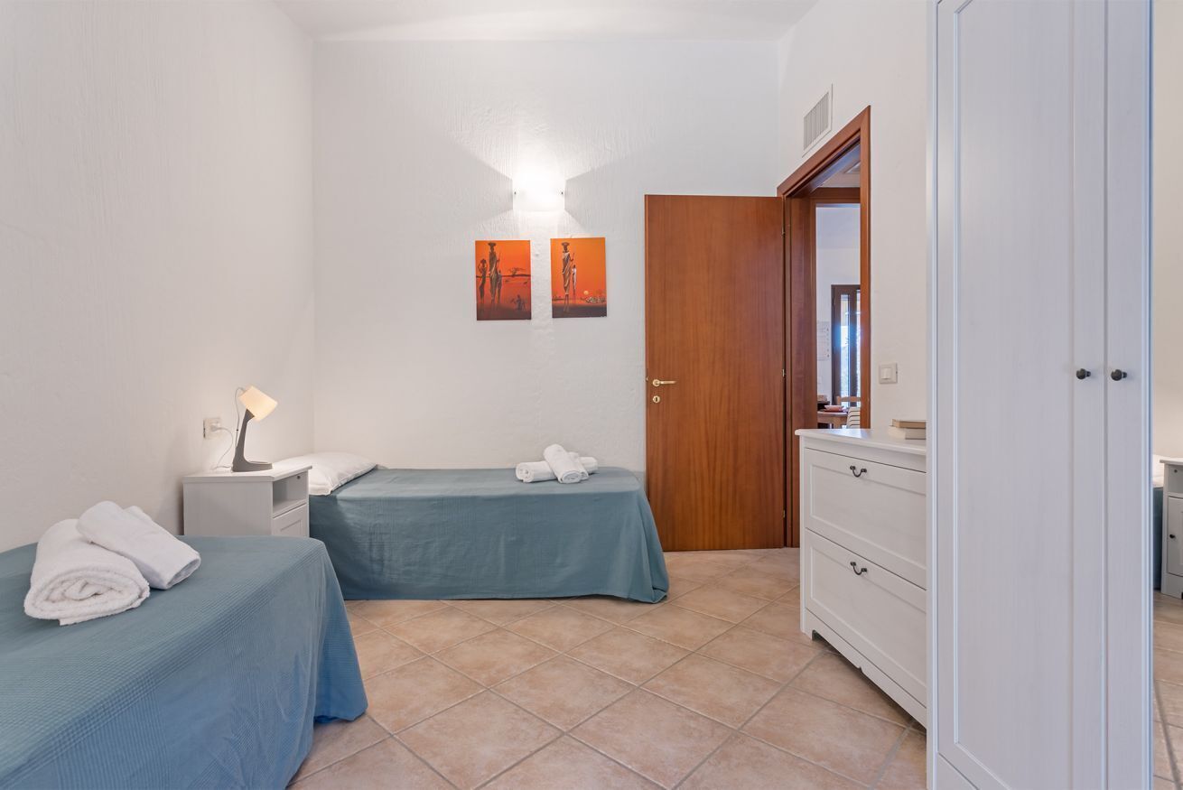A bedroom with two beds, a nightstand, a dresser, and a door.