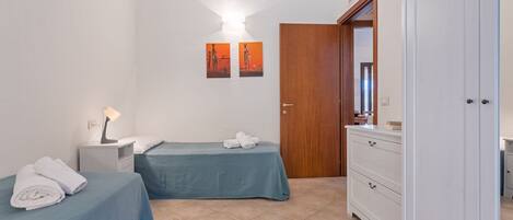 A bedroom with two beds, a nightstand, a dresser, and a door.