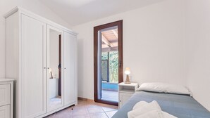 A bedroom with a bed, a nightstand, a wardrobe, and a door leading to an outdoor area. - La Casa Azzurra with shared Pool (Tertenia)