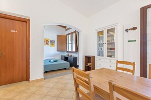 Een compacte kamer met een bed, een eettafel met stoelen, een keuken met kastjes en een eigen deur.