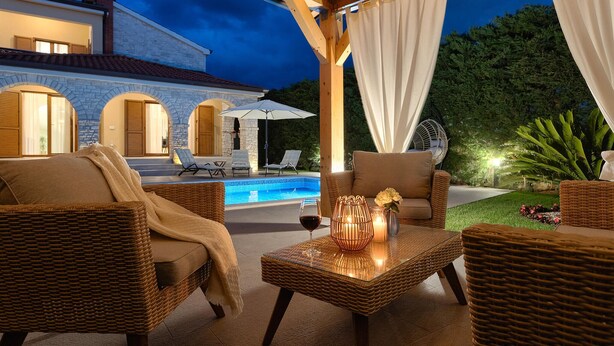 An outdoor patio with wicker furniture, a glass-top table, and a pool.