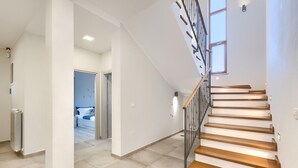A modern interior with a staircase, a visible bedroom with a bed and a window, and a radiator.