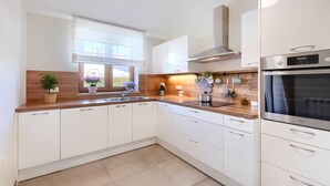 A modern kitchen with white cabinets, a stainless steel oven, and a window with potted plants.