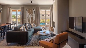 A modern living room with a sofa, armchair, and coffee table, a TV, and a large window with a view of a pool and buildings. - Awesome home in Porec (Porec)