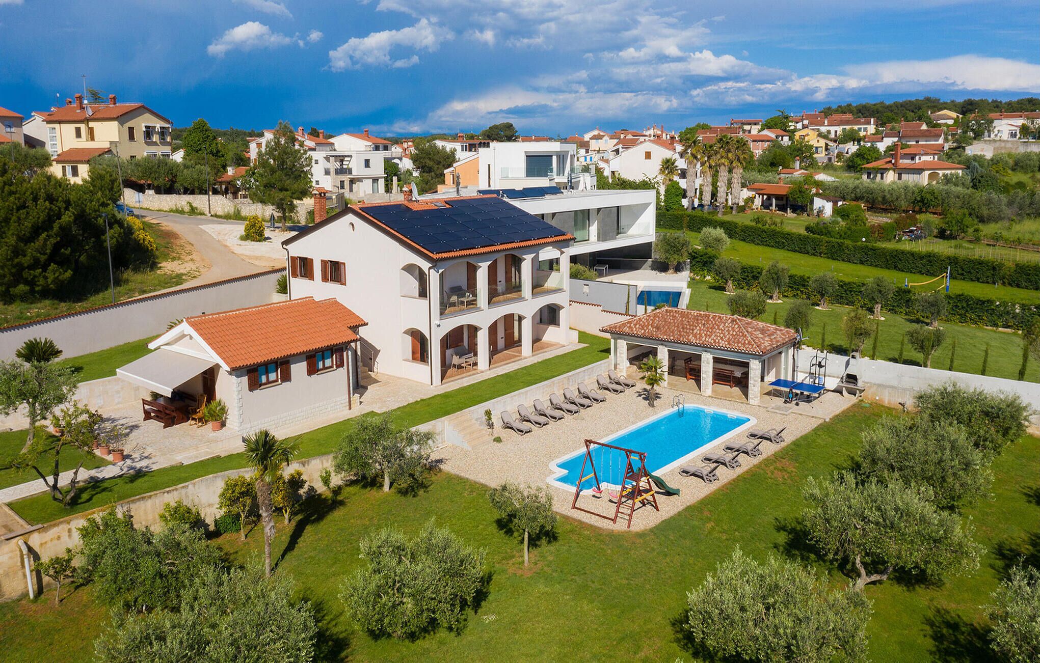 A large, modern house with a swimming pool, multiple balconies, and a well-maintained garden.