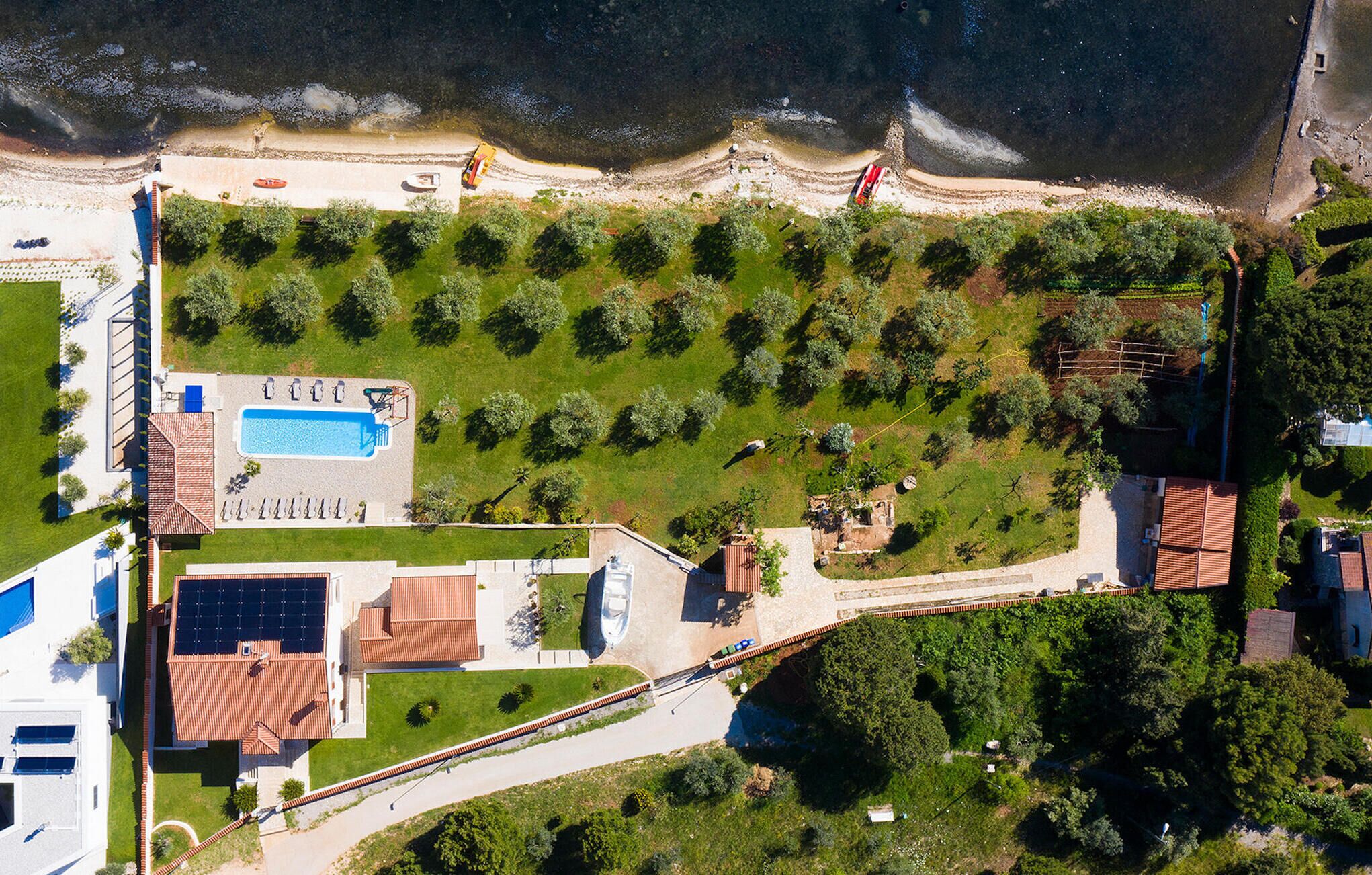 An aerial view of a coastal property with a swimming pool, solar panels, and a well-maintained garden.