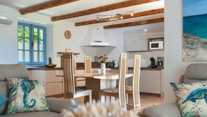 A modern living room with a wooden dining table, two sofas with patterned cushions, a kitchen area with a microwave, and a painting of a beach scene. - Pet friendly home in Pula (Pula)