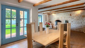 A dining area with a wooden table and chairs, a stone fireplace, and a blue door leading outside. - Pet friendly home in Pula (Pula)
