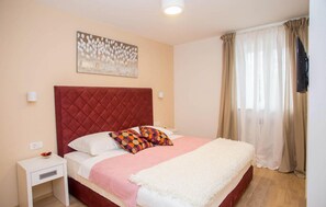 A bedroom with a red headboard, a bed with white and multicolored pillows, a white bedside table, and a beige wall with a floral artwork. - Beautiful home in Buzet with sauna (Buzet)