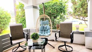 A patio area with two cushioned chairs, a glass table with a potted plant, and a hanging chair with a cushion.