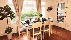 A dining area with a wooden table, white chairs, and a window with curtains.