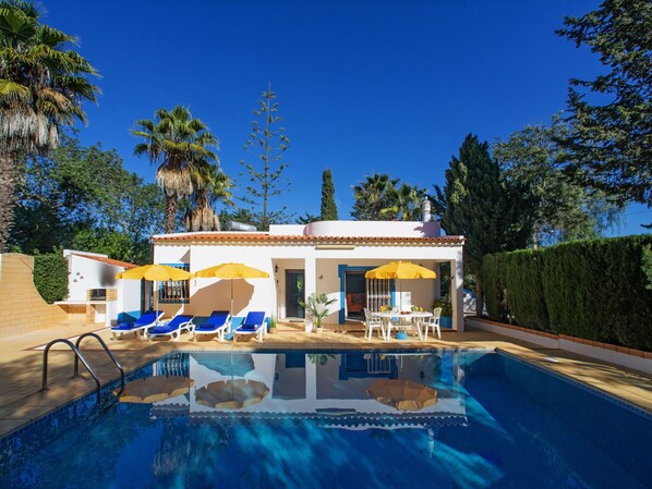 A poolside area with a pool, lounge chairs, and umbrellas.