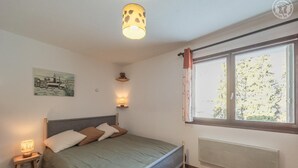 Une chambre à coucher avec un lit, des lampes de chevet, une fenêtre avec des rideaux, un radiateur et un tableau accroché au mur.