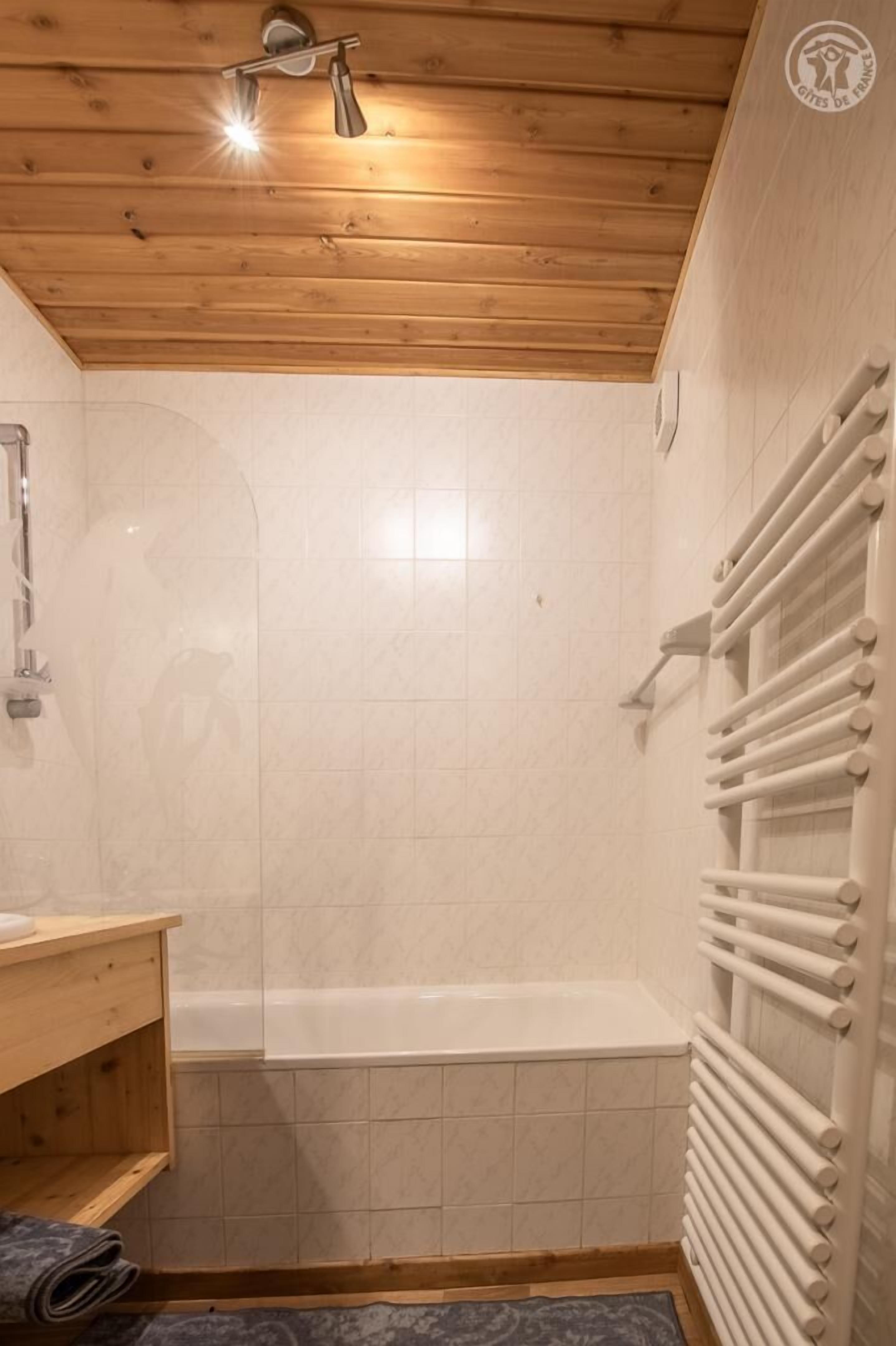 Et badeværelse med træloft, et hvidt badekar, et håndklædetørrestativ og et brusehoved.