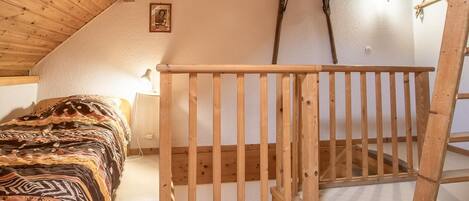 A bedroom with a wooden bunk bed, a ladder, a wall-mounted light fixture, and a framed picture on the wall.