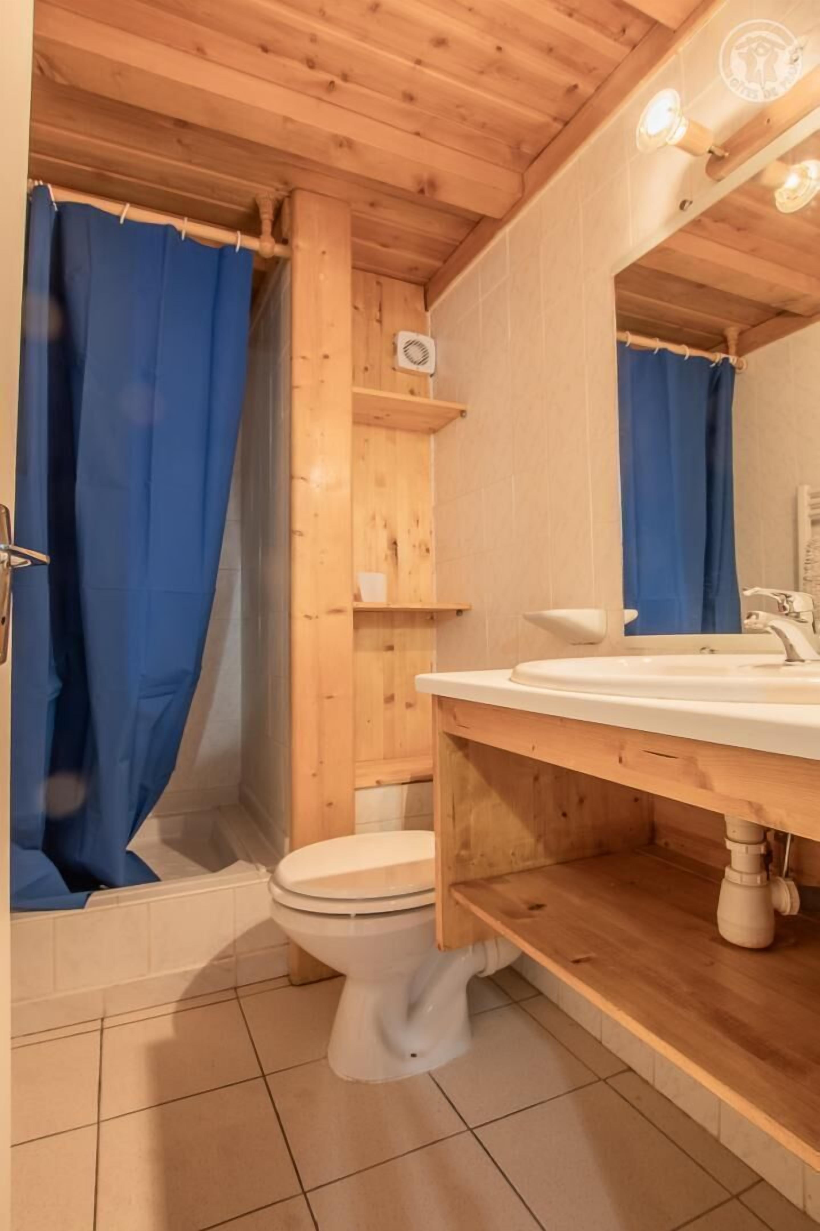 Een houten badkamer met een wit toilet, een wastafel en een douchegordijn.