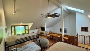 A high-ceilinged room with bunk beds, a dining table, and a ceiling fan.