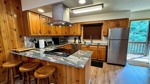 A kitchen with wooden cabinets, a granite countertop, a stainless steel refrigerator, and a bar stool area.