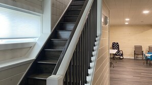 A staircase with a wooden finish and metal railings leading to a room with a wooden floor and a table with chairs. - Family friendly cottage, covered deck, close to lake to fish, swim, and boat (Whitney Point)