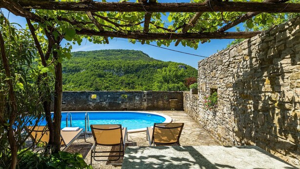 A pool area with a stone wall, two lounge chairs, and a view of a green hillside. - Stunning home in Buzet (Buzet)