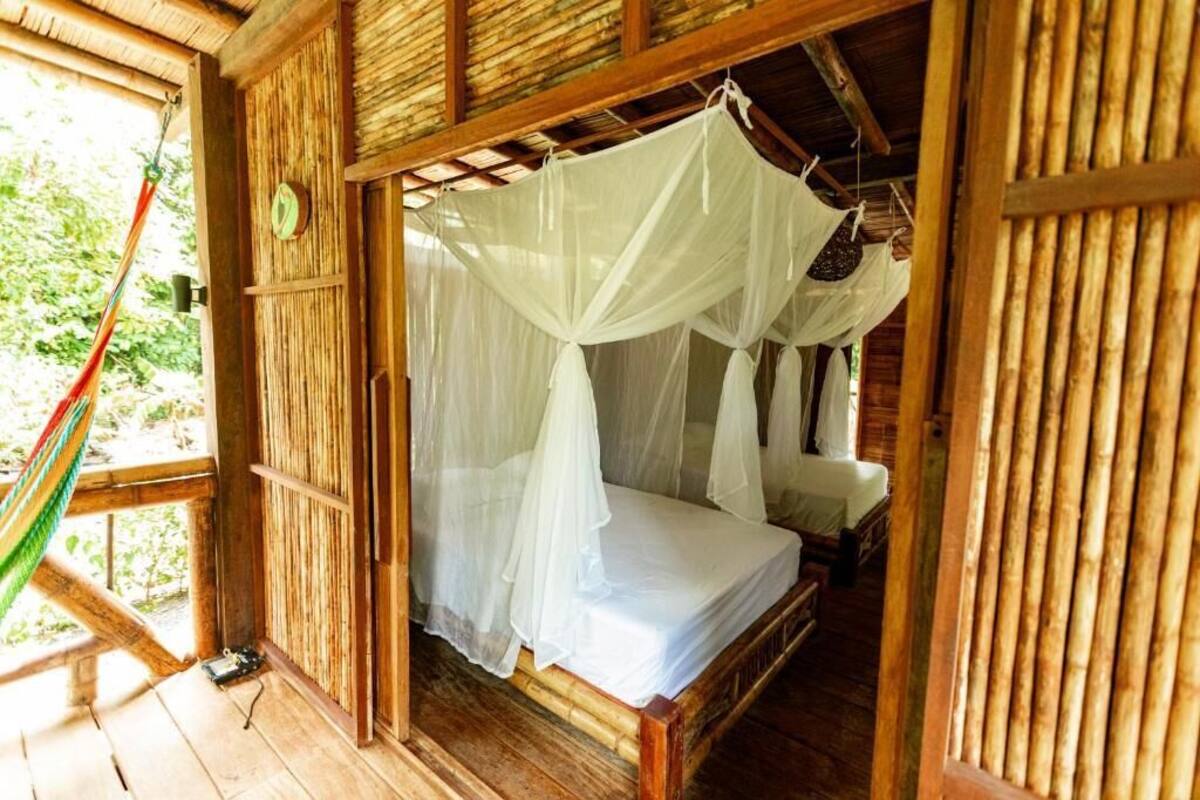 Quarto de madeira com uma cama sob um dossel branco, uma rede e teto de madeira.
