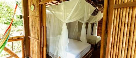 Una habitación de madera con una cama bajo un dosel blanco, una hamaca y techo de madera.